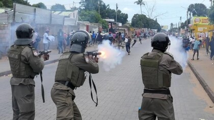 Policiais avançam e disparam contra manifestantes desarmados durante protestos de rua. A imagem traduz o clima de medo, repressão e instabilidade descrito no artigo, expondo a tensão política e social que tomou conta de Moçambique