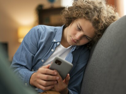 Adolescente observa atentamente a tela do celular em um momento de isolamento. A repetição de conteúdos violentos pode contribuir para dessensibilização emocional progressiva. O consumo digital na adolescência envolve mais do que entretenimento: também influencia construção ética, percepção social e desenvolvimento emocional