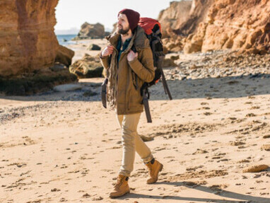 Young nomadic traveler with a backpack exploring an autumn sea coast, dressed in a warm jacket and hat