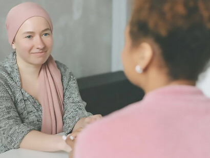 A woman with cancer and her close friend are sitting at the table and holding hands