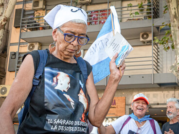 Mujer mayor en una marcha sosteniendo un ejemplar de la Constitución Argentina, usando un pañuelo blanco en la cabeza y una camiseta con el lema "El sagrado derecho a la desobediencia"
