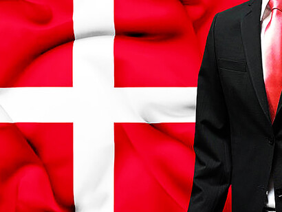 A distinguished businessman stands before the Danish flag, exuding professionalism in a crisp white shirt and a bold red tie
