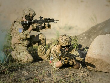 Um militar armado, equipado com uniforme de camuflagem, posiciona-se junto a uma formação rochosa, utilizando o terreno como proteção. A cena remete à importância do posicionamento estratégico e das condições de combate nas operações militares, aspectos que também influenciam o desenvolvimento da guerra na Ucrânia