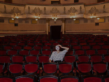 A female mime sits alone in an auditorium, engrossed in reading a manuscript, capturing the essence of solitude and creativity in performing arts