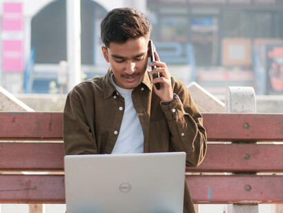 A young Indian man sits alone in a park, browsing job listings on his laptop