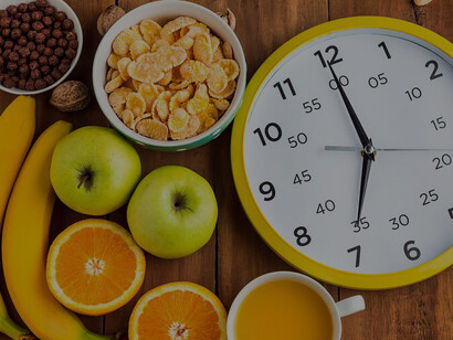 A healthy homemade breakfast featuring muesli, apples, fresh fruits, and walnuts, with a clock on the table, representing intermittent fasting