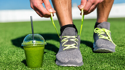 Close-up of a fitness enthusiast tying running shoes beside a green smoothie before a workout session
