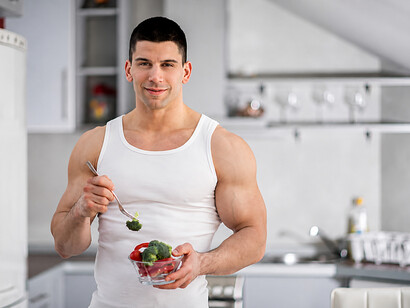 Muscular athlete in a modern kitchen preparing and eating a healthy vegan meal