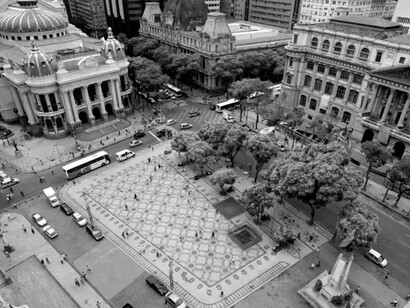 Vista aérea da Praça Floriano, no coração da Cinelândia, com o Theatro Municipal, o Museu Nacional de Belas Artes e o Palácio Pedro Ernesto compondo um dos mais importantes conjuntos arquitetônicos do Rio de Janeiro. A organização do espaço revela a permanência de um projeto urbano que atravessou diferentes períodos da história da cidade