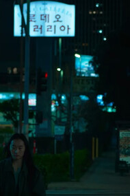Lead character Hayoung walking alongside a downtown avenue at night in So Young Shelly Yo's ''Smoking Tigers''