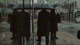 Reflection of pedestrians carrying umbrellas in a glass window facade, Bulgaria