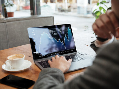 A businessman at a café, reviewing stock market trends and data while sitting at a table with his laptop