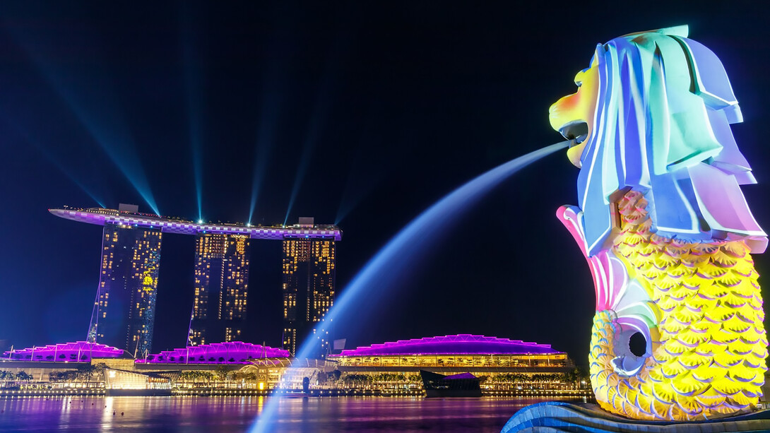 The Merlion fountain, illuminated by lights, stands proudly overlooking Singapore's iconic Marina Bay Sands