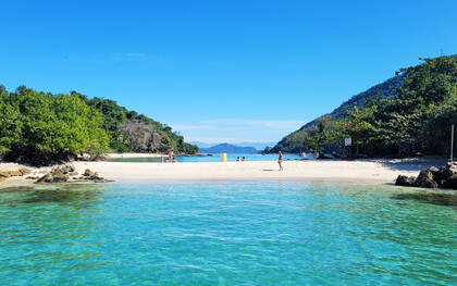 A praia aparece entre o mar, a vegetação e as montanhas ao fundo, formando uma paisagem de águas tranquilas e natureza exuberante. Em Ilha Grande, o afastamento do ritmo urbano abre espaço para desacelerar e reencontrar outros modos de estar no mundo