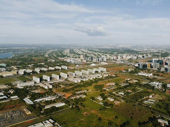 Do alto, Brasília revela o contraste entre o desenho urbano planejado e a expansão que se estende para além de seus limites. Ao fundo, as cidades-satélite aparecem distantes do núcleo original, evidenciando como o crescimento efetivo pode assumir trajetórias diferentes daquelas previstas pelo planejamento