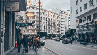 Pedestrians moving through a commercial district surrounded by Moroccan and international businesses in Tangier, Morocco, representing the diverse communities shaped by migration and mobility