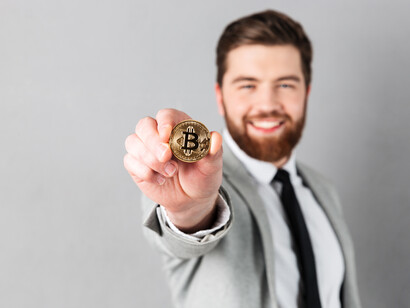 A smiling businessman in a suit holding a bitcoin, representing digital currency