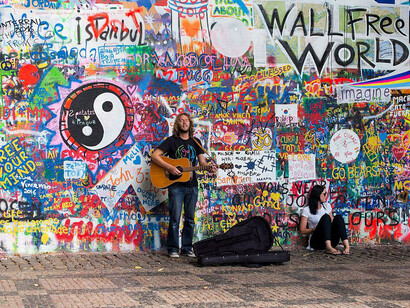 Artista cantando frente al Muro de John Lennon, que recibe este nombre al ser continuamente decorado con nuevos grafitis inspirados en su figura