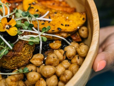 Person holding a wooden bowl filled with cooked, wholesome food