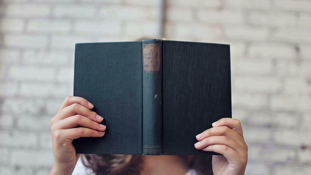 Mulher com livro aberto em frente ao rosto. Primeiro de tudo, vamos deixar claro: sim, qualquer leitura ajuda! E não, isso não é uma desculpa para se entupir de revistas de fofoca e achar que está tudo bem (apesar de que, se isso te faz feliz, quem sou eu para julgar?). O ponto é que ler, independentemente do que seja, ativa o cérebro, melhora o vocabulário e a compreensão, além de nos transportar para outros mundos e nos fazer enxergar as coisas de outra maneira
