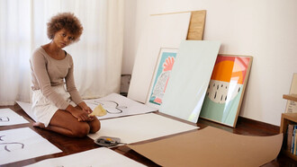 A young artist sitting on the floor surrounded by their artworks
