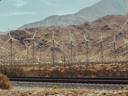 Wind turbines beside a railroad at the feet of a mountain range