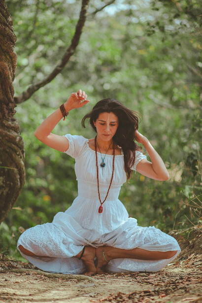 A woman squatting on the ground, lifting both hands upward as if embracing the surrounding silence and light