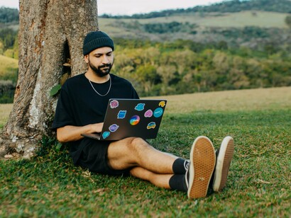 Um profissional trabalha ao ar livre com seu notebook, representando a flexibilidade dos novos modelos de trabalho. A evolução tecnológica ampliou possibilidades, mas também trouxe novos desafios para construir carreiras consistentes e relações profissionais duradouras