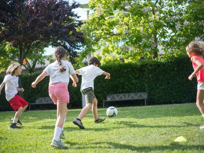 Young children playing football outdoors on a green field