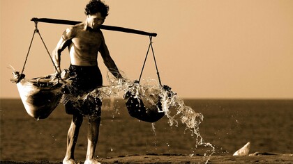 Uomo che tiene in equilibrio sulle spalle due ceste cariche: "Questo tempo moderno ci permette di vivere vite comode e di assecondare la gratificazione immediata, eppure senza impegno, senza fatica, senza sacrificio non c’è crescita"