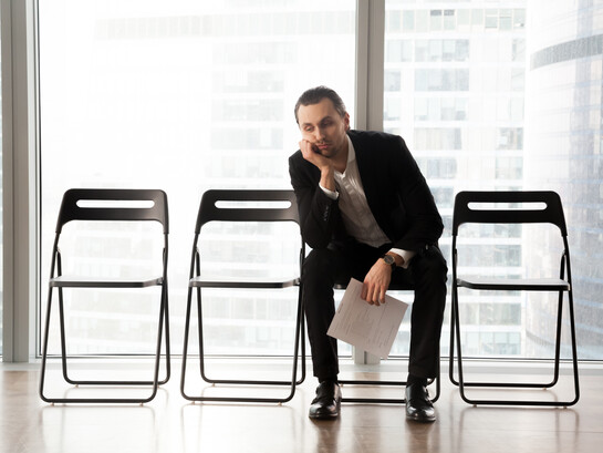 A bored young man in a suit sits in a waiting room for a job interview, looking upset
