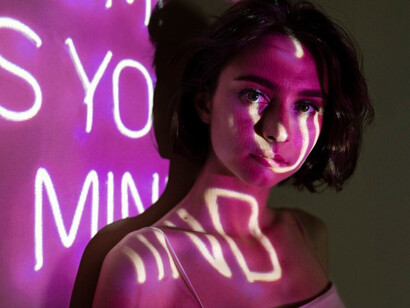 A striking portrait of a teenage woman illuminated by neon lights, captured as a still from a performance art piece