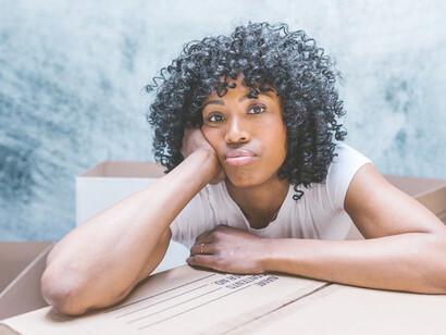 A woman, seated amidst a cluster of cardboard boxes, signifies her departure, as she prepares to move away from her current surroundings
