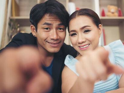 A happy Korean couple laughing and taking a selfie while sitting together on the couch at home, sharing a joyful moment of love and connection