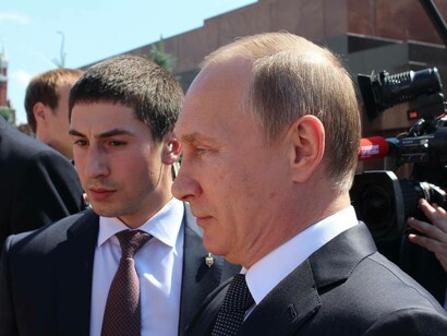 Russian President Vladimir Putin near a bodyguard with a cameraman behind him plotting his next move in his war with Ukraine