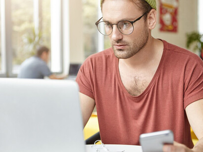 Young man in a cafe multitasking with laptop and smartphone