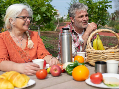 In Portugal, a senior couple enjoys a cheerful picnic with fresh fruits and vegetables in a lush garden