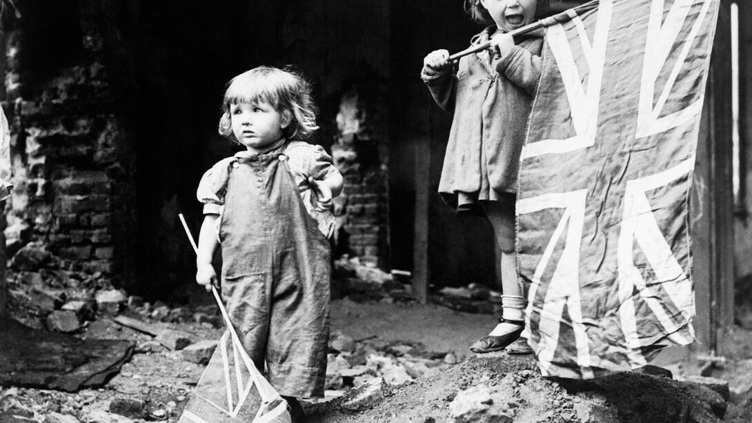 Two small girls waving their flags to celebrate the end of the war in the rubble of Battersea on VE Day