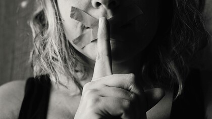 A woman places her finger on her already duck-taped lips