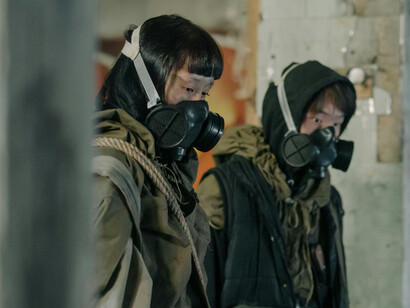Two people in gas masks in a torn building