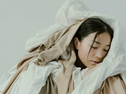Mulher cercada de peças de roupa. Com o tempo e a evolução da indústria, o mercado precisou se adaptar a uma nova realidade e aos novos hábitos de consumo. E onde entra a sustentabilidade nisso? Quando falamos de moda, o meio ambiente precisa ser levado em consideração