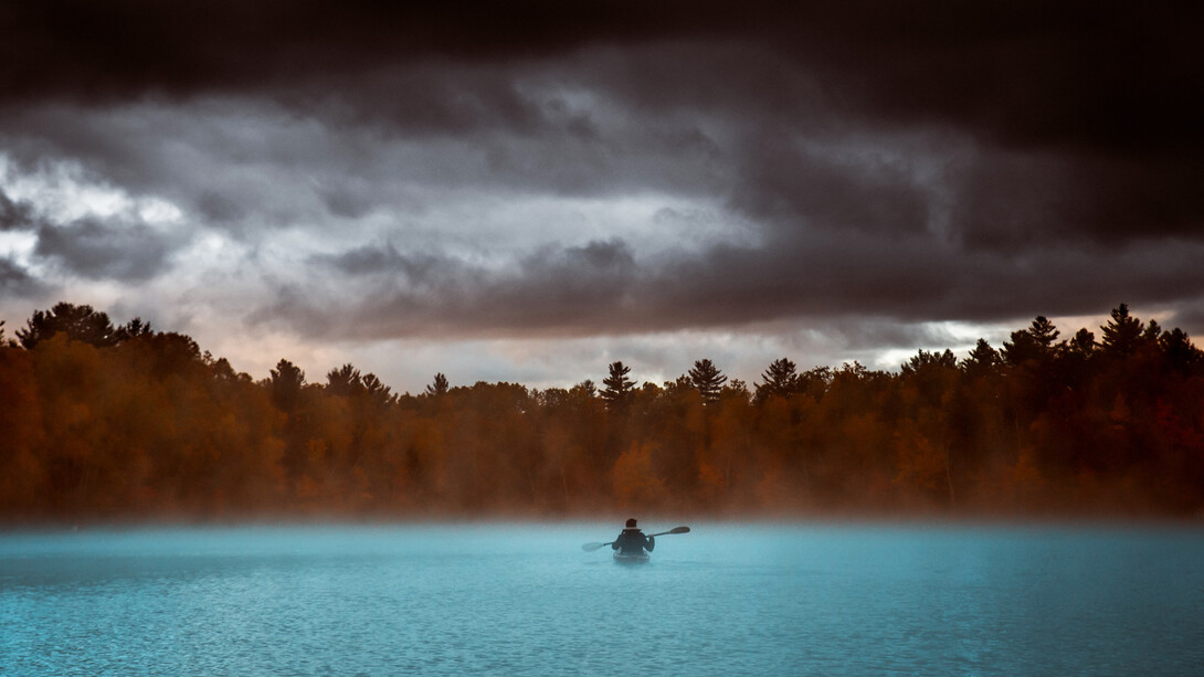 Hombre solo en un bote rema hacia un denso terreno boscoso