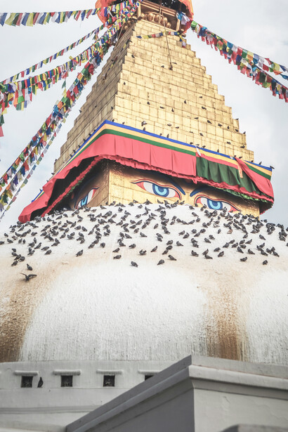 Devotees leisurely walk around the gleaming white dome of Boudhanath in Kathmandu, adorned with painted Buddha eyes, while visiting nearby monasteries and schools for prayers and seminars