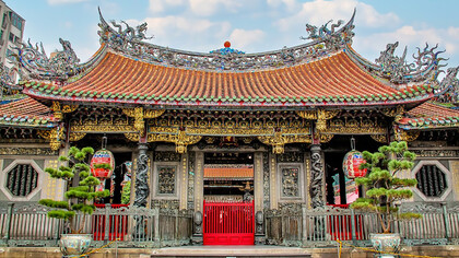 The Longshan Temple in Taipei, Taiwan, features an ancient roof adorned with dragons, set against a backdrop of a clear blue sky and fluffy white clouds