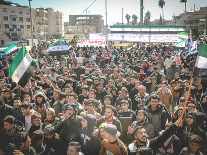 A large crowd of demonstrators waves flags and carries banners during a protest calling for freedom and justice in Idlib, Idlib Governorate, Syria
