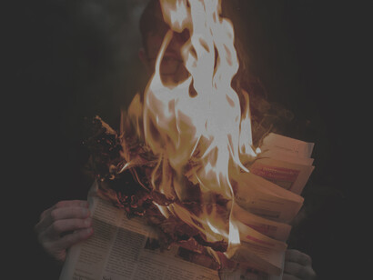A newspaper catching fire symbolizes the harmful nature of fake news