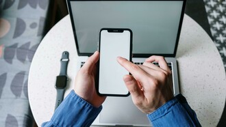 Jovem utiliza celular, relógio digital e laptop