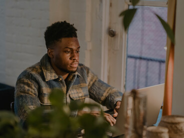 A concentrated Black man works on his laptop and drinks coffee in a café