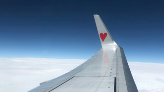 A plane's wing with a heart logo, soaring above the clouds