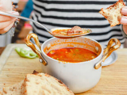 A woman eats traditional Hungarian goulash soup in a pot in an outdoor restaurant